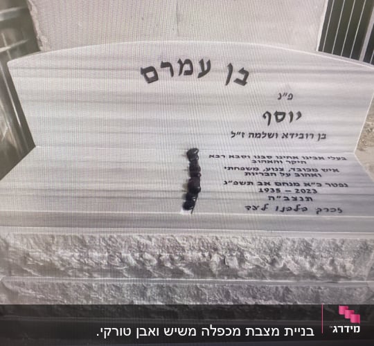 מצבה עם כיתוב בעברית ואבנים קטנות מונחות עליה